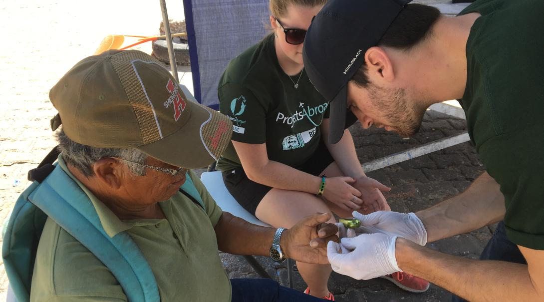 An intern screens a local for high blood sugar during a Health Fair in Belize Public Health intern tests the blood sugar levels of a patient in Belize